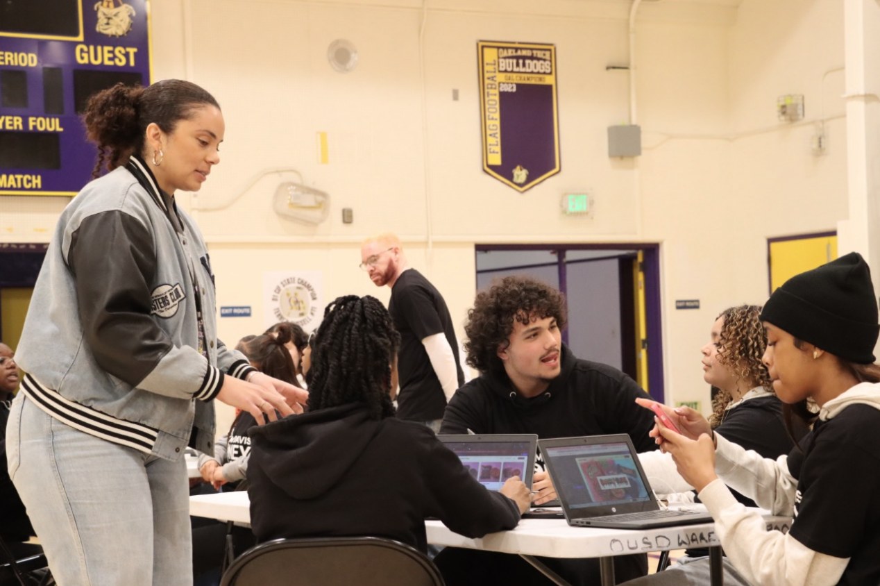 A mentor working with youth at laptops during the Oakland Tech Hackathon